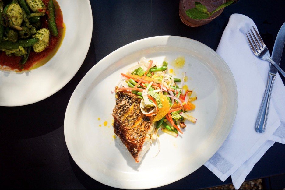 Seasonal fish entree with colorful vegetable slaw and a second plated dish on a white table at Blueprint on 3rd in Birmingham