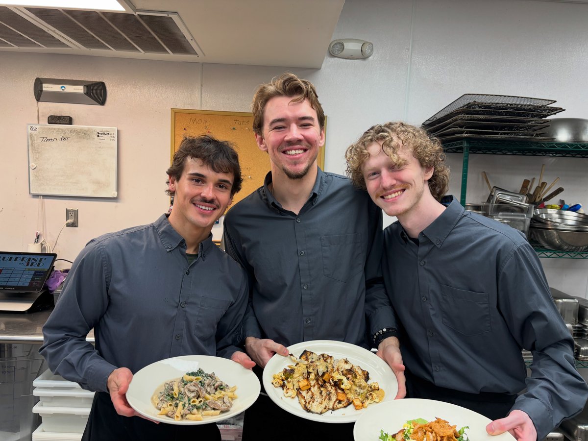 Three Blueprint on 3rd team members smiling while holding plated dishes in the kitchen