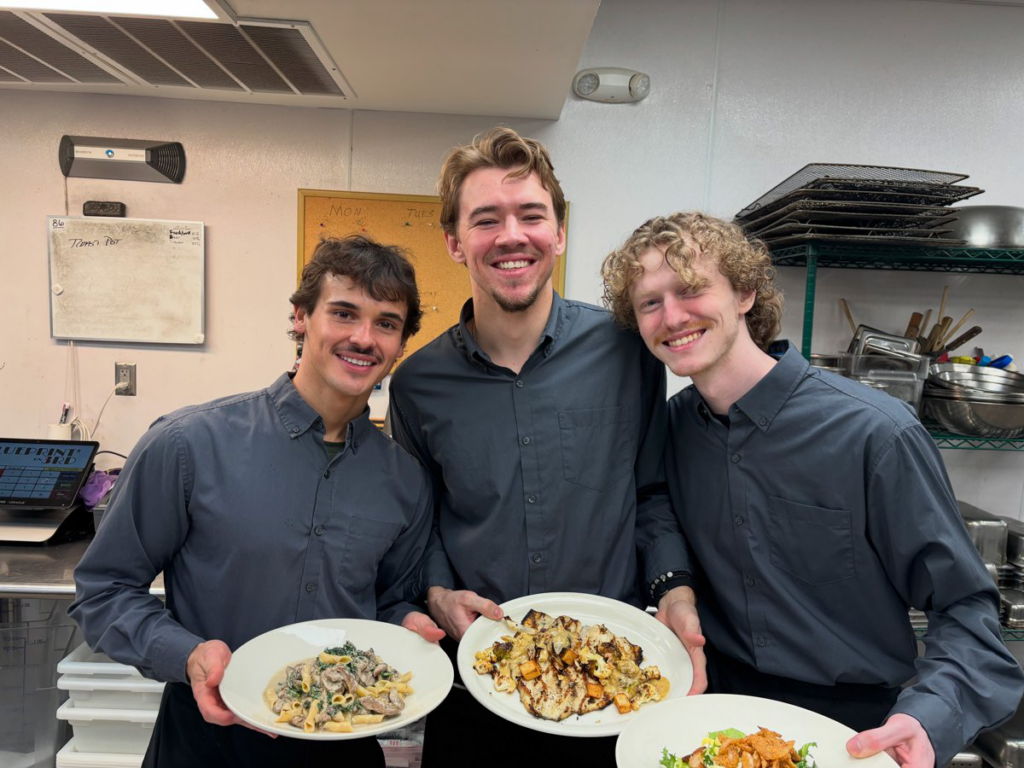 Three Blueprint on 3rd team members smiling while holding plated dishes in the kitchen