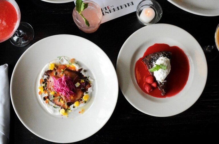 Two artfully plated dishes with colorful garnishes and craft cocktails on a dark table at Blueprint on 3rd