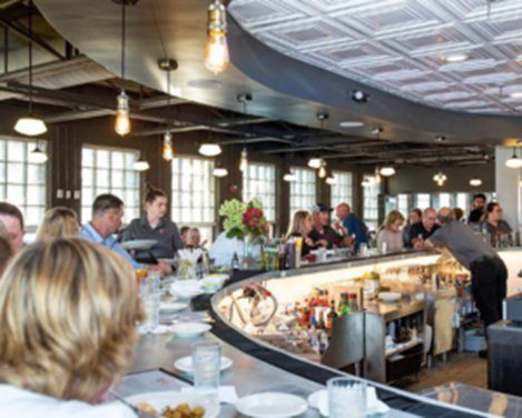 Guests gathered around a curved zinc bar beneath a pressed-tin ceiling at Blueprint on 3rd in Birmingham