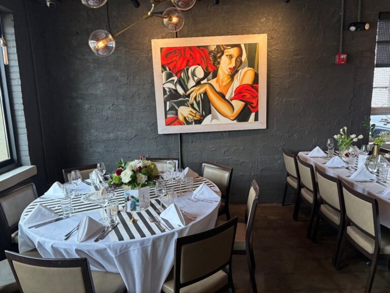 Elegantly set table with crisp linens, fresh flowers, and crystal glassware beneath a bold art deco portrait at Blueprint on 3rd