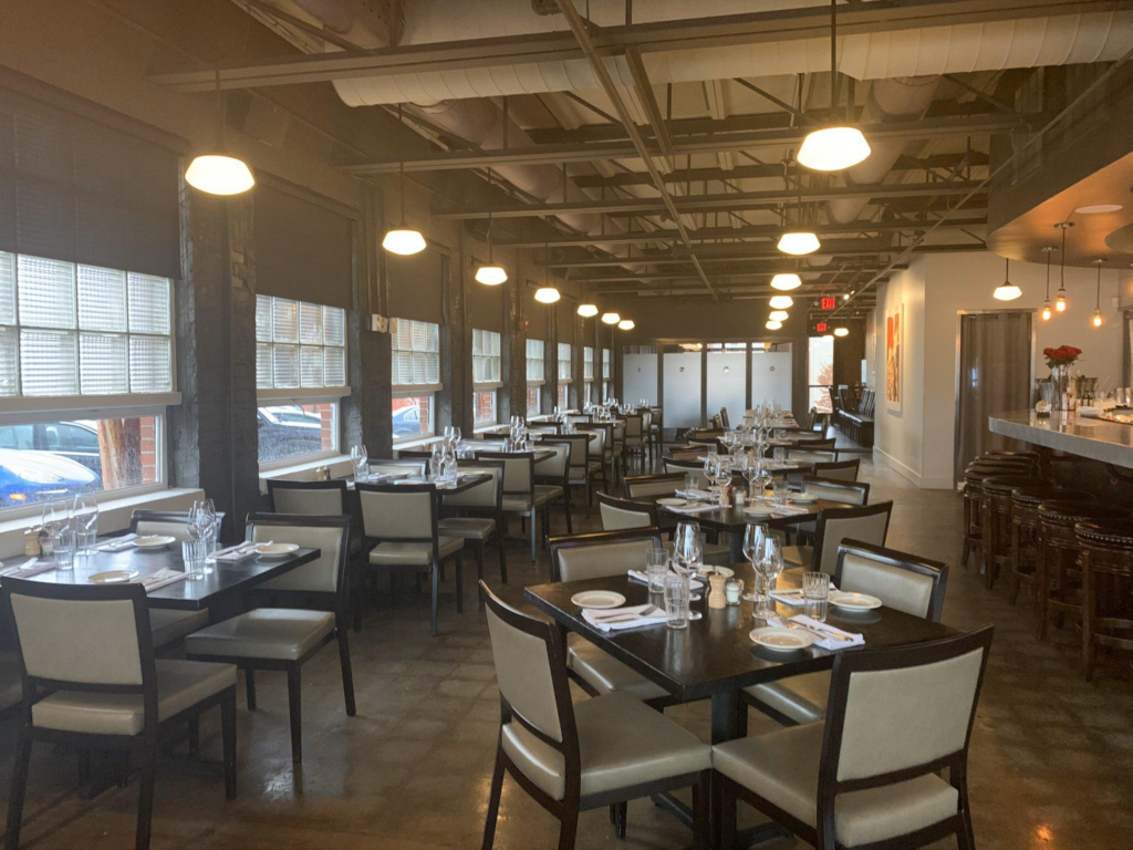 Main dining room at Blueprint on 3rd in Birmingham with set tables, exposed industrial ceiling, and the bar visible in the background